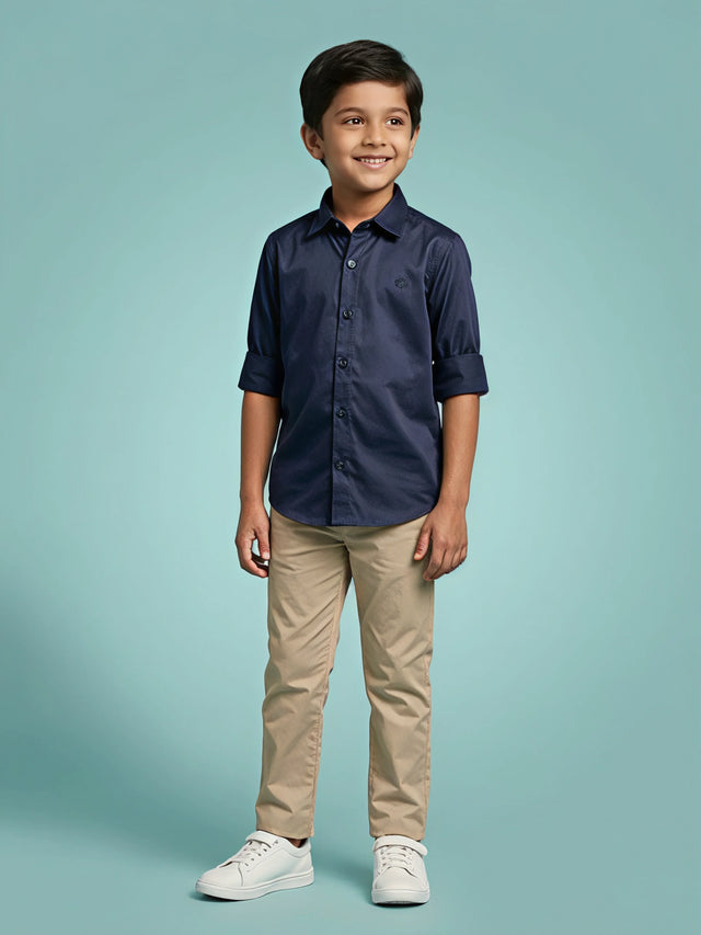 Young boy wearing a stylish navy blue casual shirt with roll-up sleeves and beige trousers