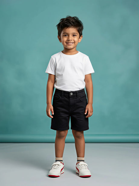 A young boy wearing a white t-shirt and black casual denim shorts with front pockets and button closure, standing against a teal background.