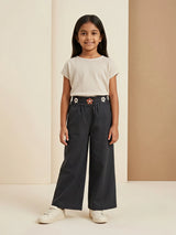Young girl wearing black wide-leg casual pants with floral embellishments on the waistband and a plain beige t-shirt
