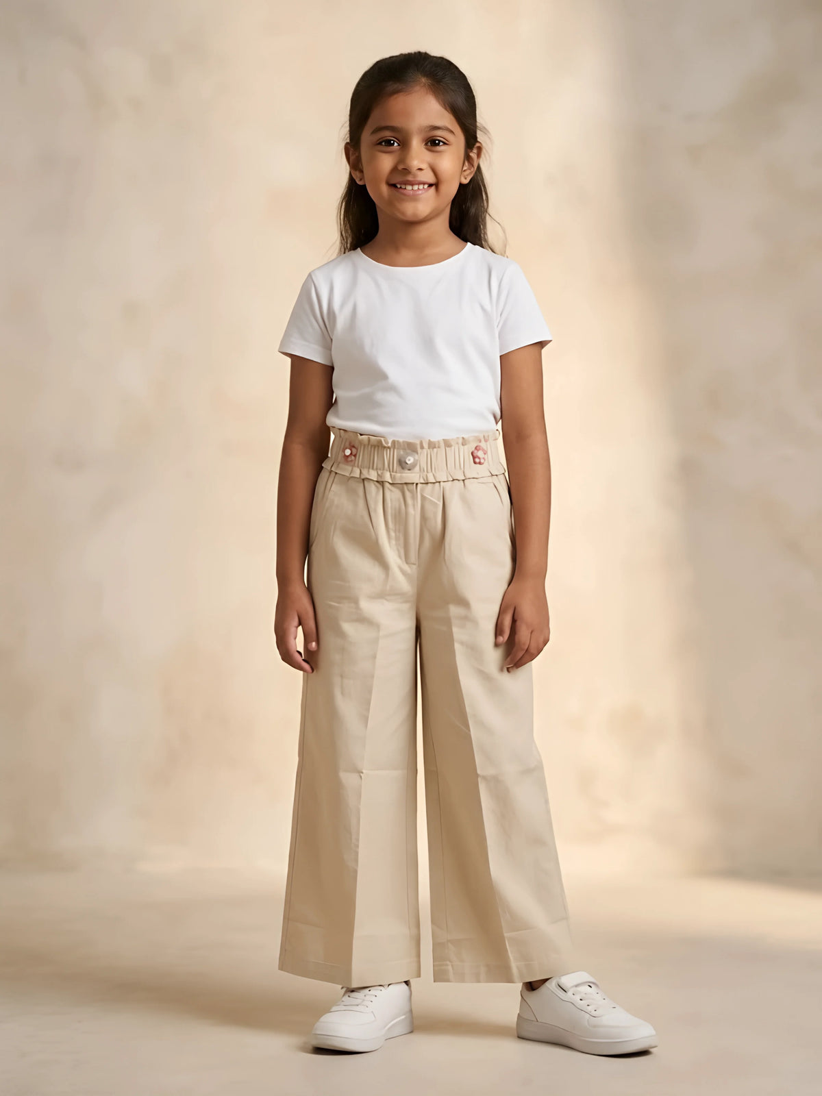 Young girl wearing cream paperbag waist casual trousers paired with a white t-shirt and white sneakers