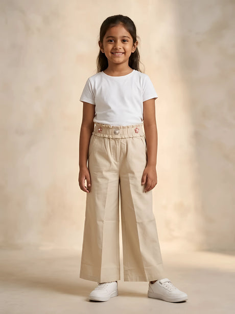 Young girl wearing cream paperbag waist casual trousers paired with a white t-shirt and white sneakers
