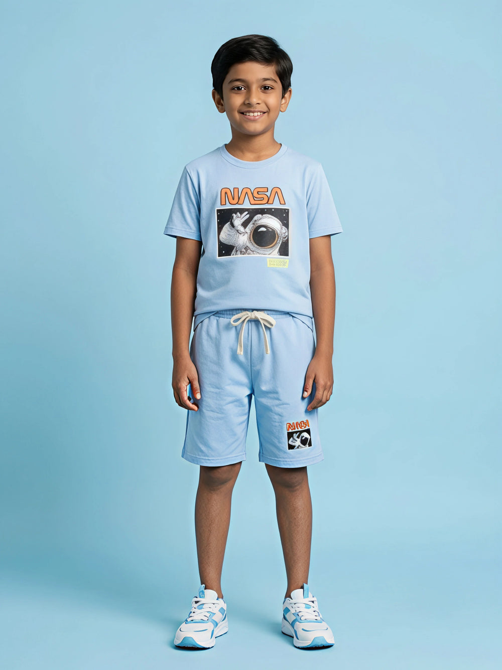 A young boy wearing a light blue matching coordinate set featuring a NASA astronaut graphic t-shirt and shorts with a drawstring, pictured in image_3c0020.jpg.