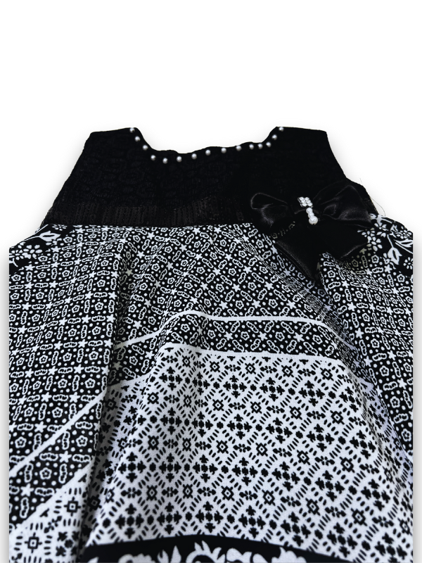 Black and white patterned girls' handkerchief hem frock with a black velvet-look bow and pearl trim on a white background.

Export to Sheets
