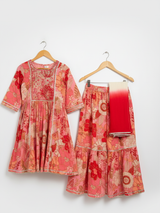 Girls' three-piece ethnic suit in a coral and peach floral print, consisting of a tiered Kurti, matching Garara, and a white-to-red ombre dupatta.