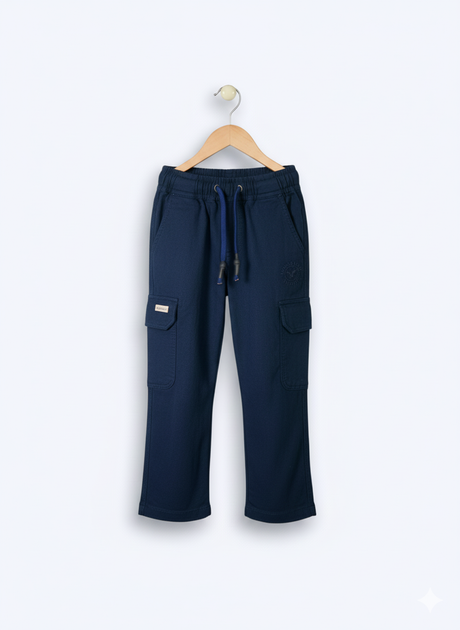Boys' plain navy blue cargo pants made of soft fleece or knit material, hanging on a wooden hanger, showing the elastic waist and large side pockets.