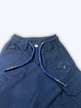 Boys' plain navy blue cargo pants made of soft fleece or knit material, hanging on a wooden hanger, showing the elastic waist and large side pockets.