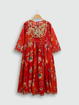 Full set laid flat: an orange/red floral-printed kurta with gold embroidered neckline, a matching tiered maxi skirt with tassels, and a printed dupatta with tassels.