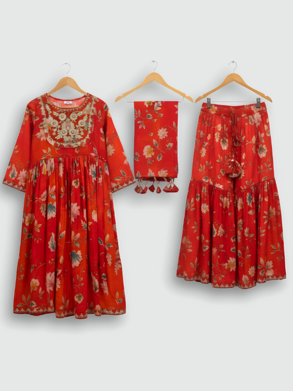 Full set laid flat: an orange/red floral-printed kurta with gold embroidered neckline, a matching tiered maxi skirt with tassels, and a printed dupatta with tassels.