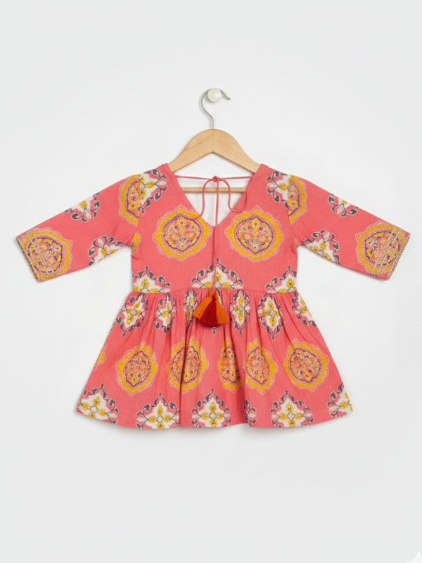 Full set laid flat: a coral pink Angrakha-style kurta with yellow/gold print and multi-colored pompoms, and matching tiered sharara pants with the same geometric print.