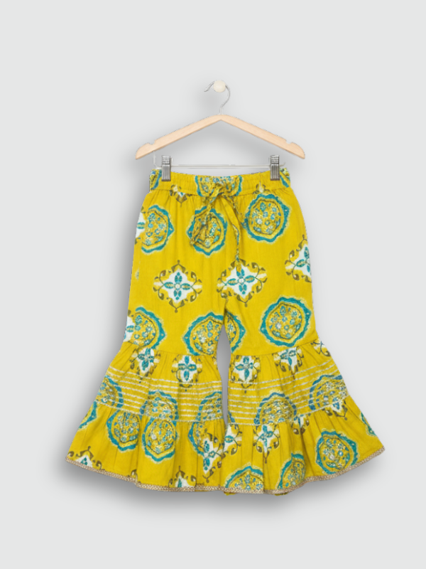 Full-length image of a young girl wearing a lime green and white floral-printed ethnic set with an embroidered peplum kurta, tiered sharara pants with a zig-zag print, and a white and green dupatta.