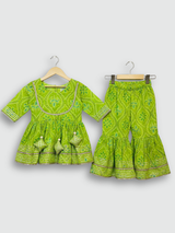 Full-length image of a young girl wearing a lime green and white floral-printed ethnic set with an embroidered peplum kurta, tiered sharara pants with a zig-zag print, and a white and green dupatta.