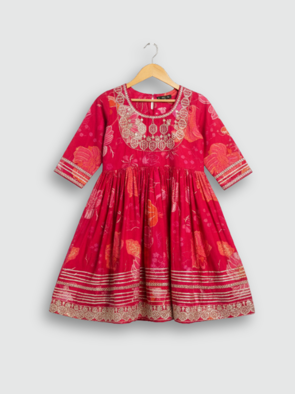 Full-length image of a young girl wearing a vibrant rani pink floral-printed ethnic set with an embroidered sleeveless peplum top, tiered sharara pants, and a pink-to-green ombre dupatta.