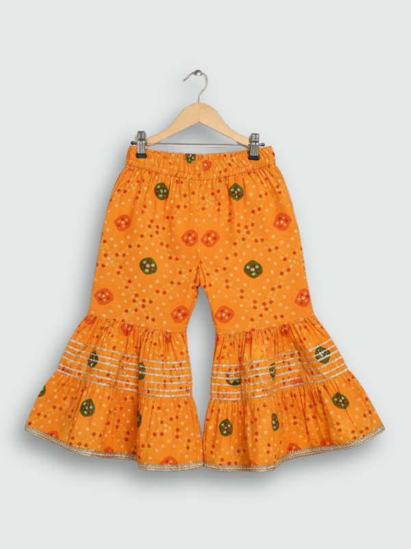Full set laid flat: a bright orange Bandhani-style printed Angrakha kurta and matching tiered gharara pants with gold and silver metallic lace trimming.