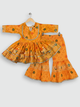 Full set laid flat: a bright orange Bandhani-style printed Angrakha kurta and matching tiered gharara pants with gold and silver metallic lace trimming.