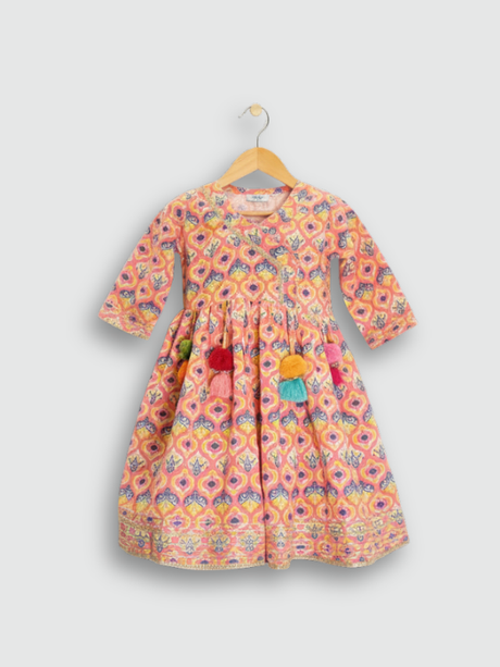 Full set laid flat: a coral pink Angrakha-style kurta with yellow/gold print and multi-colored pompoms, and matching tiered sharara pants with the same geometric print.