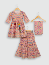 Full set laid flat: a coral pink Angrakha-style kurta with yellow/gold print and multi-colored pompoms, and matching tiered sharara pants with the same geometric print.