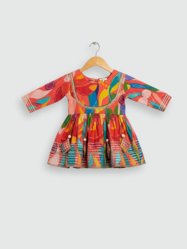 Full-length image of a young girl wearing a pink and white floral-printed ethnic set with an embroidered peplum top, tiered geometric sharara pants, and a white and pink ombre dupatta.