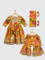 Full set laid flat: a mustard yellow Angrakha-style kurta with multicolor floral print and gold embroidery, tiered ruffle sharara pants, and a coordinating printed dupatta with tassels.
