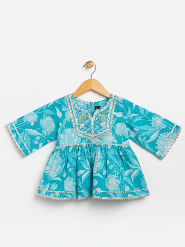 Full-length image of a young girl wearing a turquoise and blue tie-dye ethnic set with an embroidered sleeveless peplum top, tiered gharara pants with a zig-zag print, and a white-to-blue ombre dupatta.