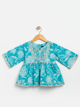 Full-length image of a young girl wearing a turquoise and blue tie-dye ethnic set with an embroidered sleeveless peplum top, tiered gharara pants with a zig-zag print, and a white-to-blue ombre dupatta.