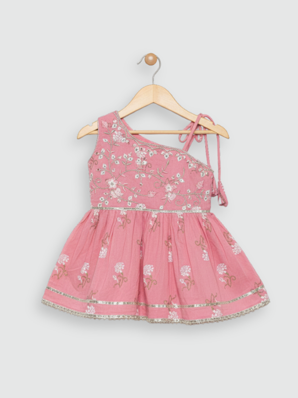 Full-length image of a young girl wearing a powder pink ethnic set with an embroidered sleeveless peplum top, tiered gharara pants with a geometric print, and a pink-to-white ombre dupatta.