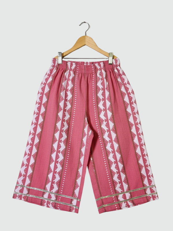 Full-length image of a young girl wearing a powder pink ethnic set with an embroidered sleeveless peplum top, tiered gharara pants with a geometric print, and a pink-to-white ombre dupatta.