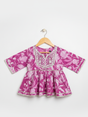 Front view of a girls' 3/4 sleeve magenta and white floral-printed peplum top (kurti) with a heavily embroidered and silver-trimmed yoke, hanging on a wooden hanger.