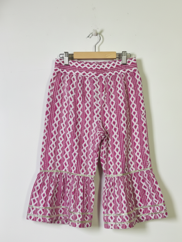 Front view of a girls' 3/4 sleeve magenta and white floral-printed peplum top (kurti) with a heavily embroidered and silver-trimmed yoke, hanging on a wooden hanger.