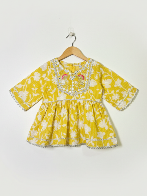 Front view of a girls' yellow and white floral-printed peplum top (kurti) with 3/4 sleeves and a heavily embroidered neckline detailed with mirror work, hanging on a white background.
