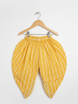 Full-length image of a young girl wearing a yellow ethnic set with a white floral print Angrakha-style top, chevron print dhoti pants, and a white-to-yellow ombre dupatta.