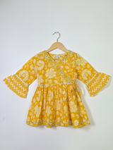 Full-length image of a young girl wearing a yellow ethnic set with a white floral print Angrakha-style top, chevron print dhoti pants, and a white-to-yellow ombre dupatta.