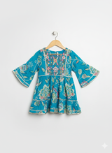 Full-length image of a young girl wearing a turquoise and blue floral-printed ethnic set with a flared kurta, tiered gharara pants, and a vibrant pink and blue ombre chiffon dupatta.