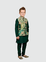 Young boy posing in a full-sleeve forest green kurta and churidar, layered with a printed Nehru-style waistcoat featuring traditional motifs, and wearing matching embellished footwear.