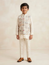 A young boy wearing a cream full sleeve shirt, matching trousers, and a printed ethnic waistcoat