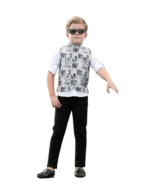 Young boy posing in a long-sleeve deep maroon velvet Indo-Western coat/sherwani with a silver embroidered crest on the shoulder, paired with white trousers and black formal shoes.