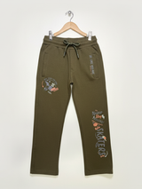 Full-length image of olive green boys' track pants with skate-themed graphics hanging on a white wall.

Export to Sheets