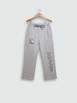 Full-length image of light grey boys' track pants with skate-themed graphics hanging on a wooden hanger against a neutral background.