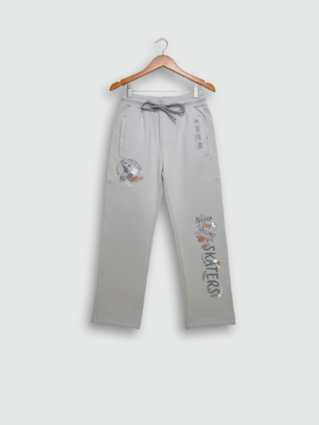 Full-length image of light grey boys' track pants with skate-themed graphics hanging on a wooden hanger against a neutral background.