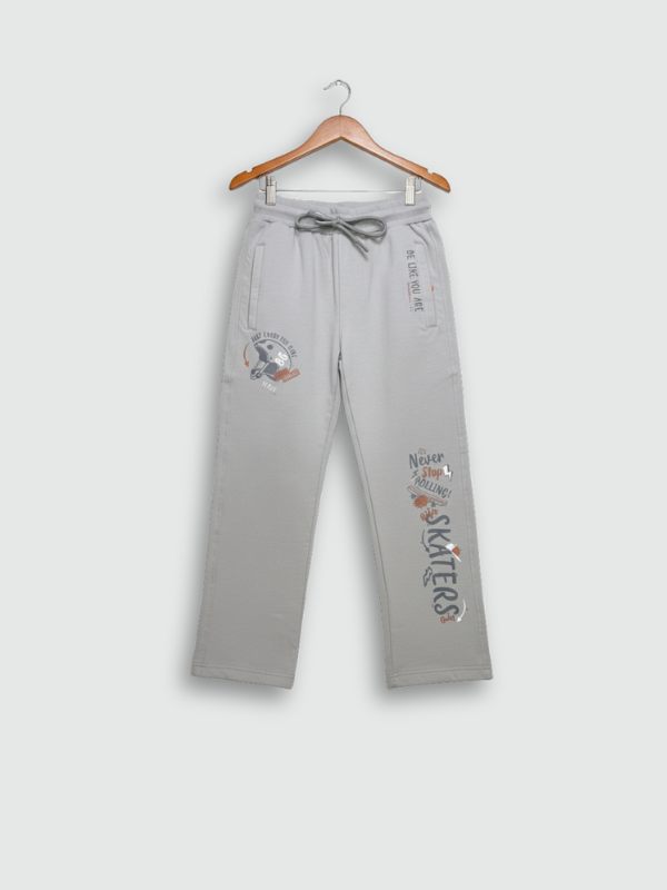 Full-length image of light grey boys' track pants with skate-themed graphics hanging on a wooden hanger against a neutral background.